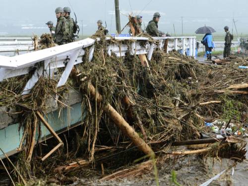 Japan's Ground Self-Defense Force personnel look at trees carried by floodwater following heavy rain in Aso, Japan. (AAP)