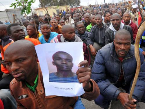 A miner carries a photo of a killed miner as thousands of striking workers singing and carrying sticks march on a South African mine in Marikana on September. (Getty Images)