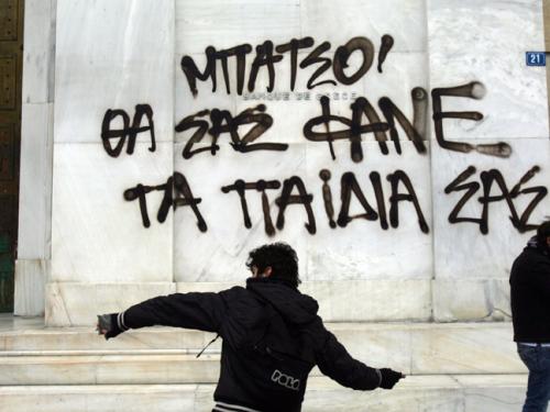 A protester throws a stone in front of graffiti that says 'cops you will be eaten by your kids' during a large demonstration in Athens (Getty)